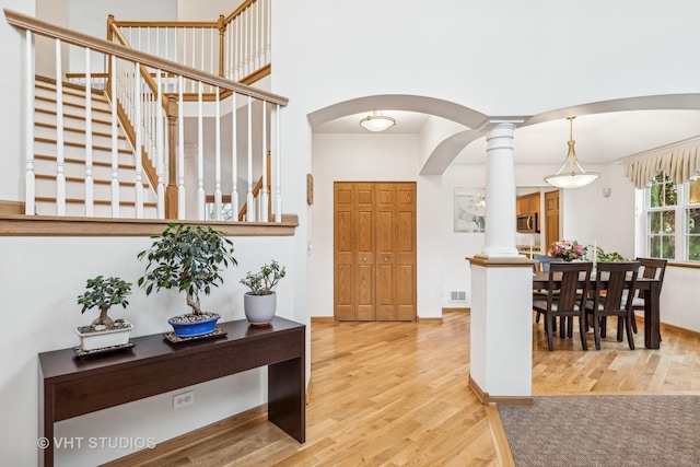 foyer entrance with light wood-type flooring, decorative columns, visible vents, and arched walkways