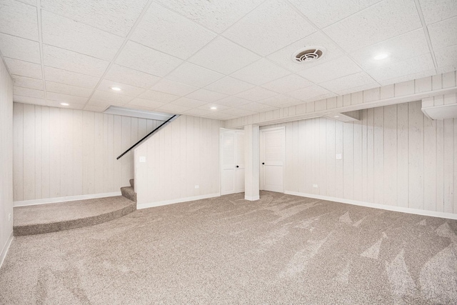 basement with carpet flooring, a drop ceiling, and wooden walls