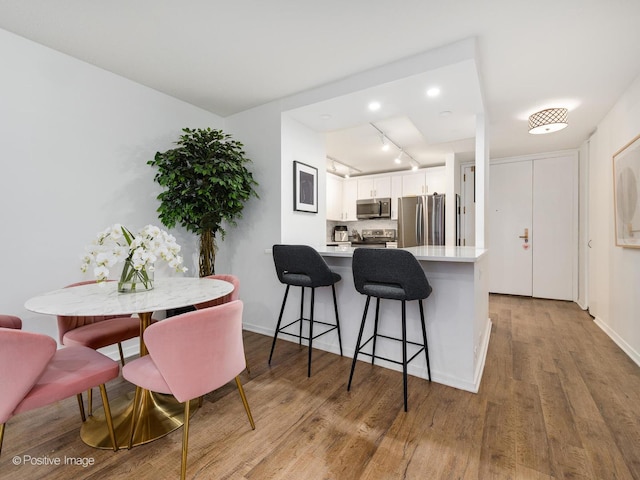 kitchen featuring kitchen peninsula, a breakfast bar area, track lighting, stainless steel appliances, and white cabinets