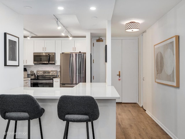 kitchen with kitchen peninsula, a kitchen bar, stainless steel appliances, and white cabinetry