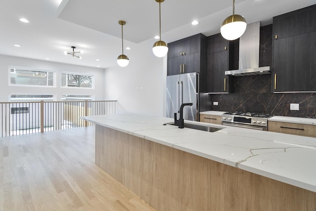 kitchen featuring wall chimney exhaust hood, decorative light fixtures, stainless steel appliances, sink, and light stone counters