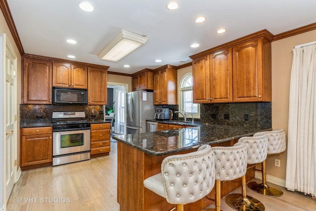 kitchen with stainless steel appliances, dark stone counters, a kitchen breakfast bar, kitchen peninsula, and ornamental molding