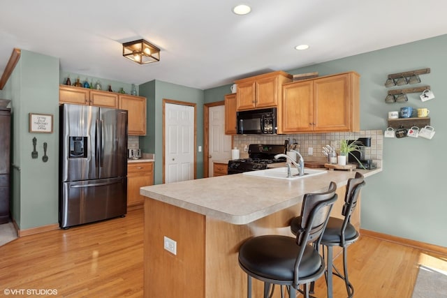 kitchen featuring a kitchen breakfast bar, black appliances, decorative backsplash, kitchen peninsula, and light wood-type flooring