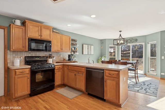 kitchen with black appliances, sink, hanging light fixtures, kitchen peninsula, and light hardwood / wood-style flooring