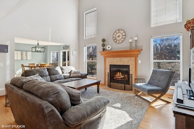 living room featuring a tiled fireplace, a high ceiling, a chandelier, and light hardwood / wood-style flooring