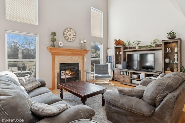 living room featuring a towering ceiling, light hardwood / wood-style floors, and a tile fireplace