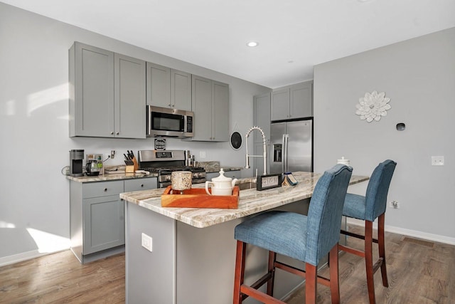 kitchen featuring appliances with stainless steel finishes, light stone countertops, a center island with sink, and gray cabinetry