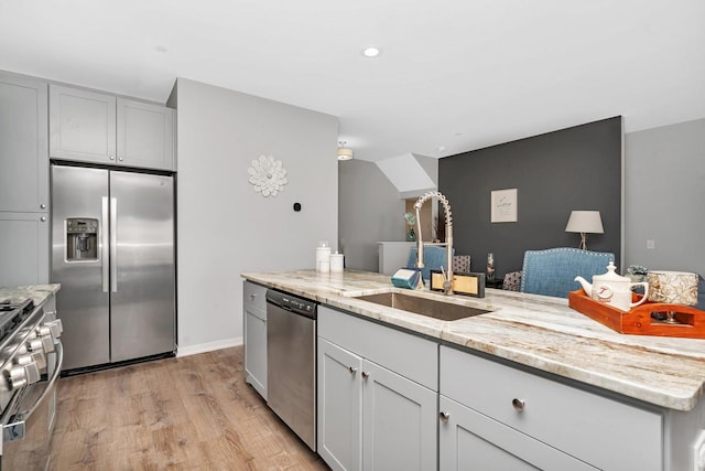 kitchen with sink, light stone counters, light hardwood / wood-style flooring, a kitchen island, and stainless steel appliances