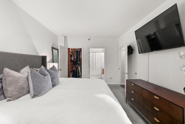 bedroom featuring ensuite bath, a walk in closet, a closet, and dark colored carpet