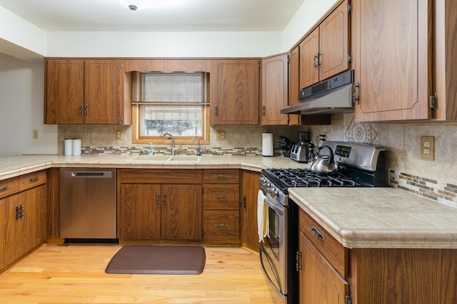 kitchen with sink, tile countertops, stainless steel appliances, and light wood-type flooring