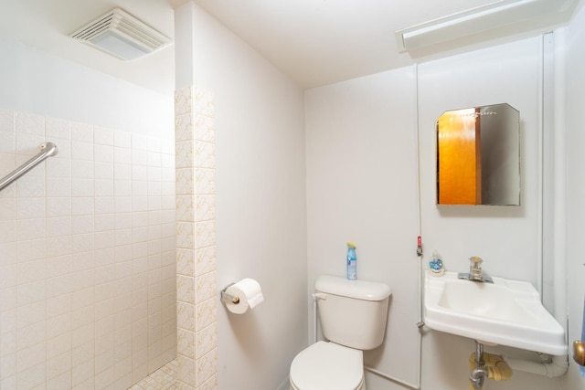 bathroom with sink, a tile shower, and toilet