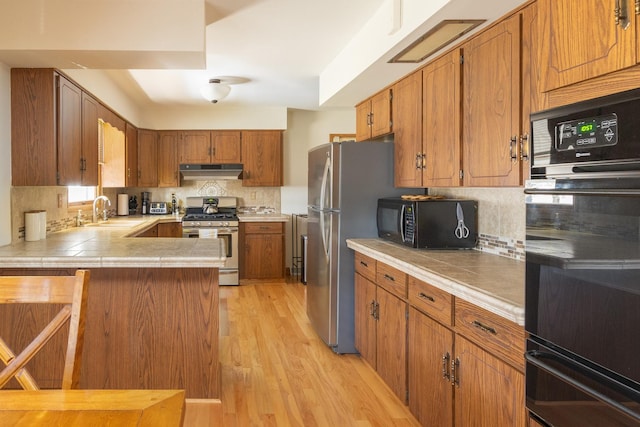 kitchen with sink, tasteful backsplash, black appliances, kitchen peninsula, and light wood-type flooring