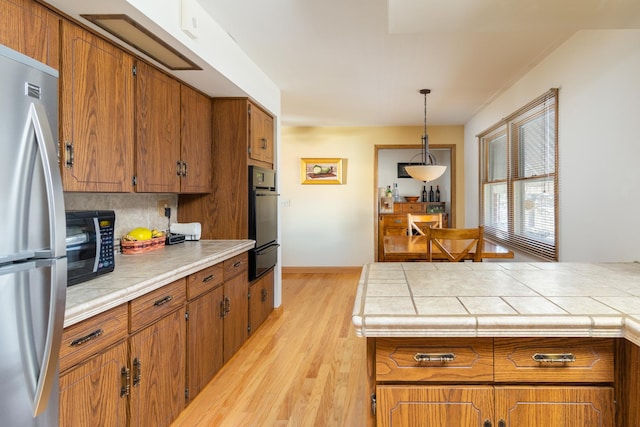 kitchen with tile countertops, decorative light fixtures, light hardwood / wood-style floors, decorative backsplash, and black appliances