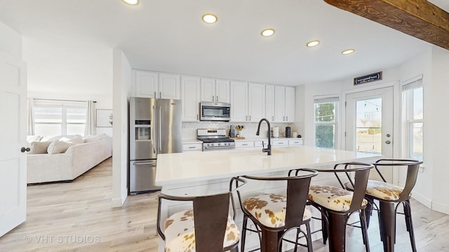 kitchen featuring light hardwood / wood-style flooring, a breakfast bar area, appliances with stainless steel finishes, white cabinets, and a center island with sink