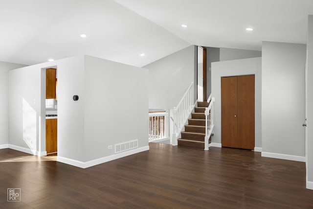 unfurnished living room with visible vents, baseboards, stairs, vaulted ceiling, and dark wood-style floors