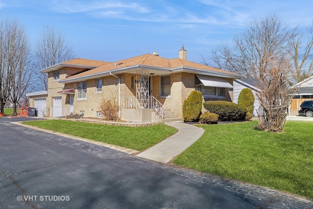 view of front of house with a front yard, driveway, a chimney, a garage, and brick siding