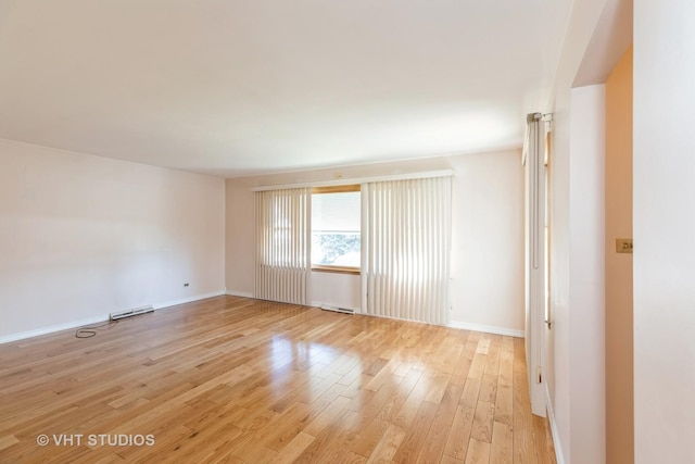 empty room with visible vents, light wood-style flooring, baseboards, and a baseboard radiator