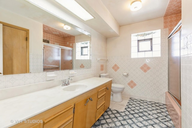 full bath featuring tile patterned floors, toilet, tile walls, bath / shower combo with glass door, and vanity