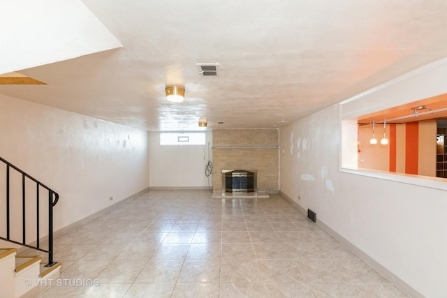 basement with visible vents, baseboards, light tile patterned flooring, a fireplace, and stairs