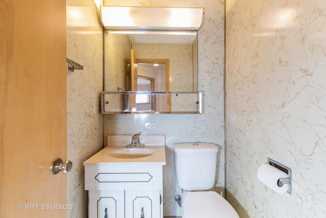 half bathroom with toilet, wallpapered walls, and vanity