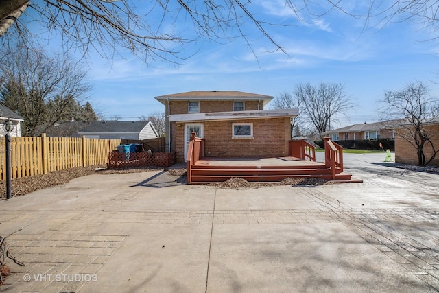 back of house featuring brick siding, a deck, driveway, and fence