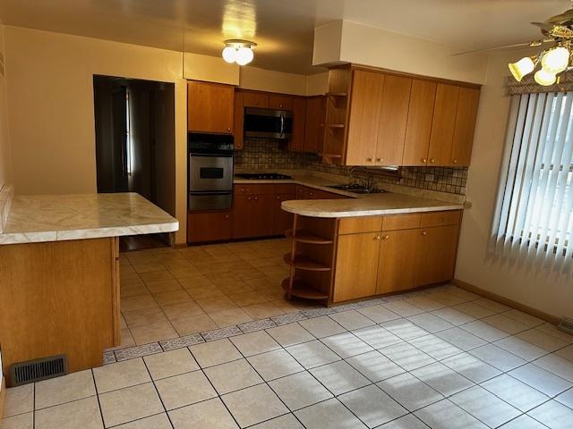 kitchen featuring backsplash, light tile patterned flooring, kitchen peninsula, and appliances with stainless steel finishes