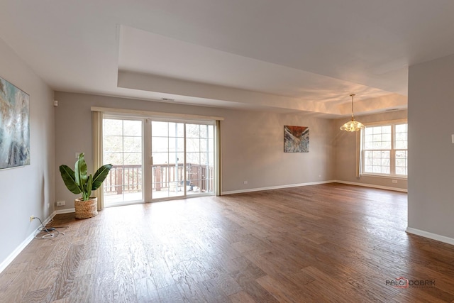 spare room with a raised ceiling, a chandelier, and hardwood / wood-style floors