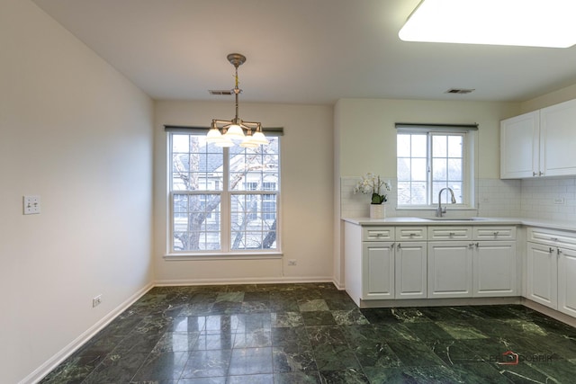 kitchen with an inviting chandelier, decorative backsplash, plenty of natural light, white cabinets, and sink