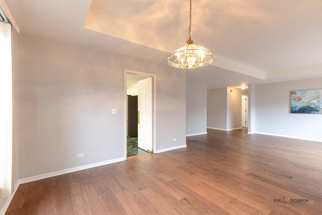 empty room with wood-type flooring, a tray ceiling, and a notable chandelier