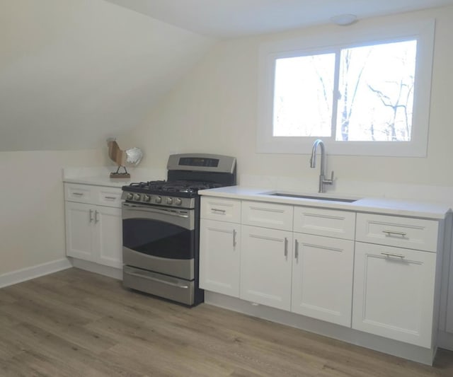 kitchen featuring lofted ceiling, sink, white cabinetry, light hardwood / wood-style flooring, and stainless steel gas range