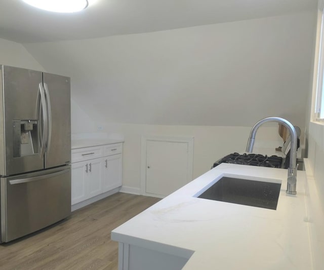 kitchen featuring vaulted ceiling, sink, light wood-type flooring, stainless steel fridge with ice dispenser, and white cabinets