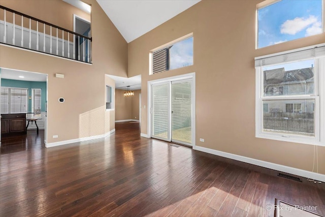 unfurnished living room with a high ceiling, an inviting chandelier, a healthy amount of sunlight, and dark hardwood / wood-style floors