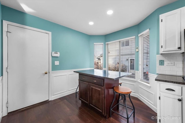 kitchen featuring dark hardwood / wood-style floors, a kitchen island, white cabinets, and a breakfast bar