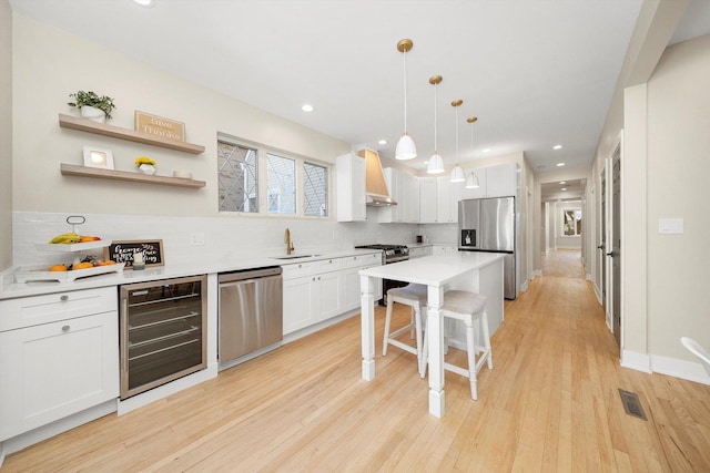 kitchen with appliances with stainless steel finishes, decorative light fixtures, white cabinetry, wine cooler, and premium range hood