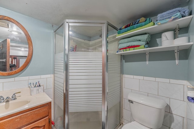 bathroom featuring toilet, vanity, tile walls, and a shower with shower door