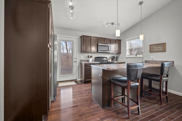 kitchen with vaulted ceiling, pendant lighting, dark wood-type flooring, stainless steel appliances, and dark brown cabinets