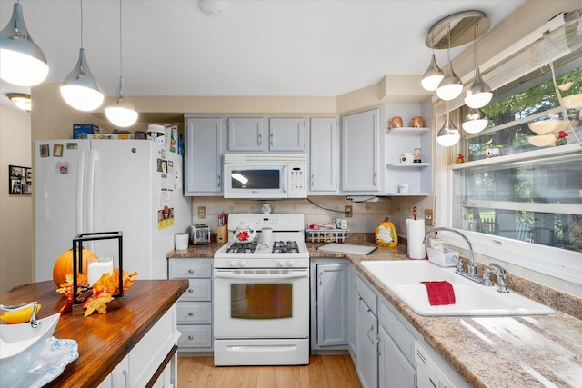 kitchen with hanging light fixtures, white appliances, light stone countertops, and sink