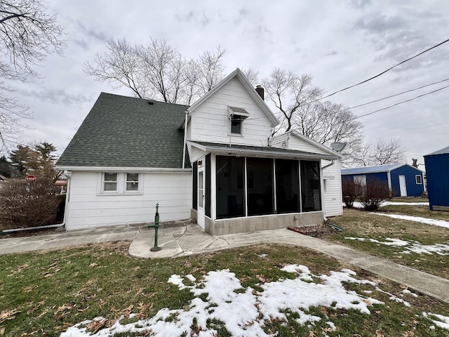 snow covered back of property with a patio, a sunroom, and a lawn