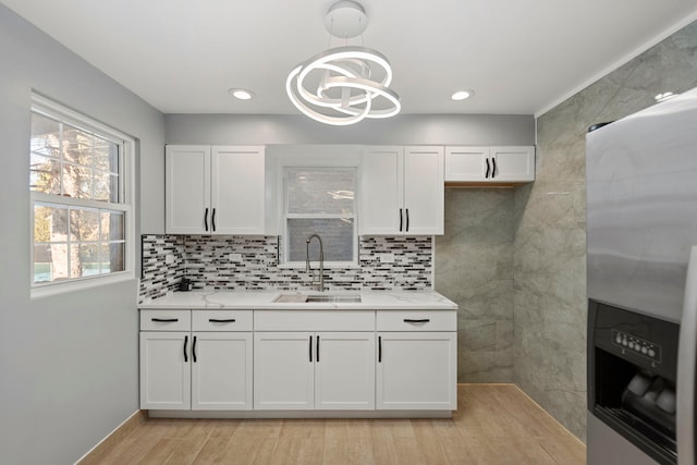 kitchen featuring sink, stainless steel refrigerator with ice dispenser, light stone counters, white cabinets, and decorative light fixtures