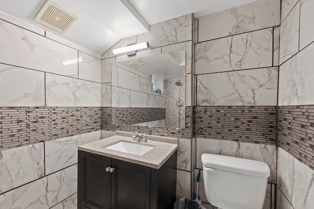 bathroom featuring vanity, vaulted ceiling, tile walls, and toilet