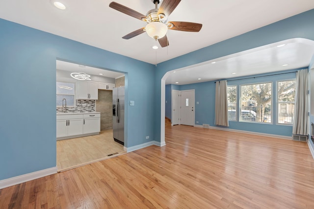 unfurnished living room with sink, ceiling fan, and light wood-type flooring