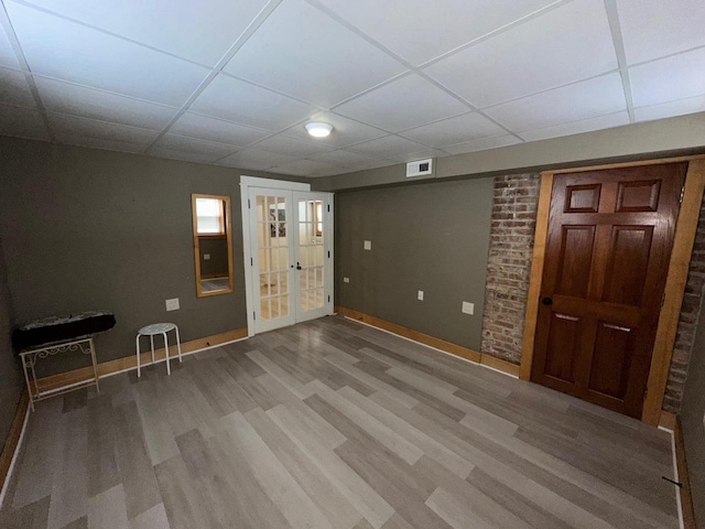 basement featuring a drop ceiling, hardwood / wood-style floors, and french doors