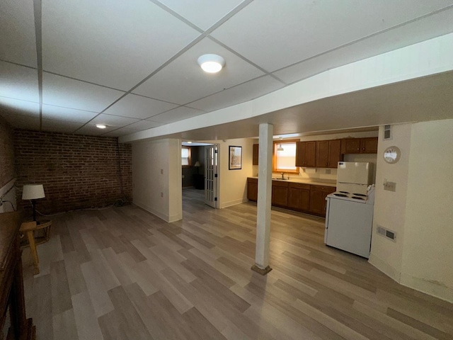 basement with brick wall, sink, a paneled ceiling, and light hardwood / wood-style floors