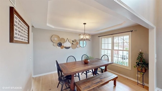 dining space with a tray ceiling, a chandelier, and light hardwood / wood-style flooring