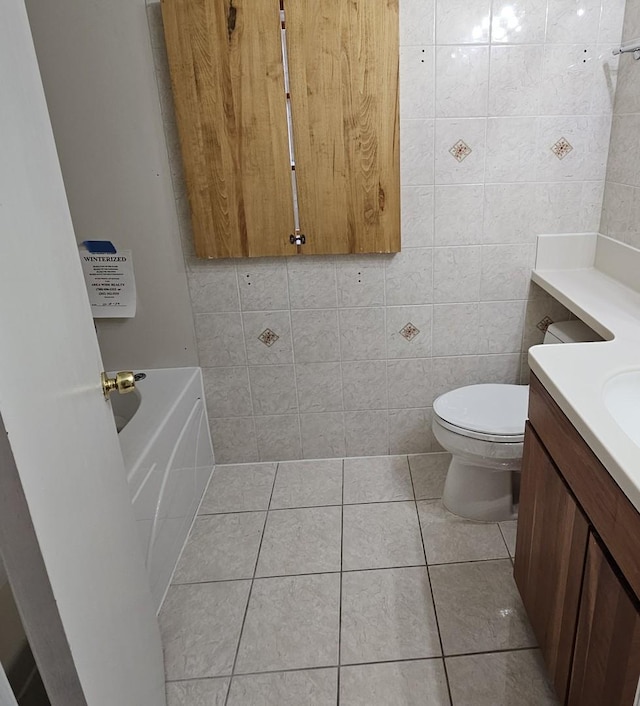 bathroom featuring toilet, vanity, tile patterned flooring, tile walls, and a bath