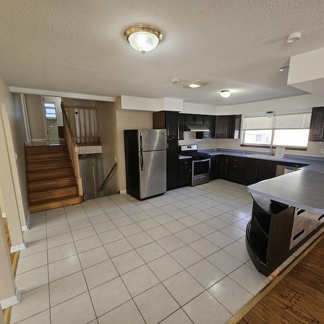 kitchen featuring a textured ceiling, stainless steel appliances, sink, backsplash, and light tile patterned floors