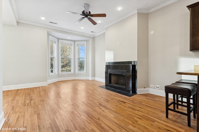 living room with a tiled fireplace, ornamental molding, ceiling fan, and light wood-type flooring