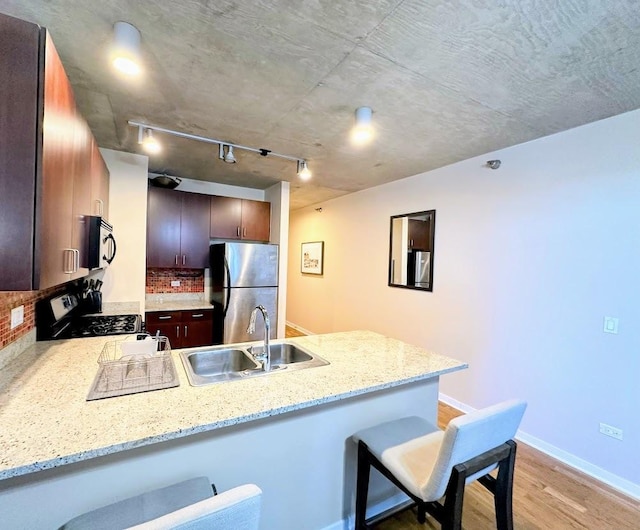 kitchen with decorative backsplash, sink, kitchen peninsula, a breakfast bar, and stainless steel appliances