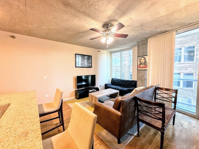 living room with a wall of windows, ceiling fan, and light hardwood / wood-style flooring