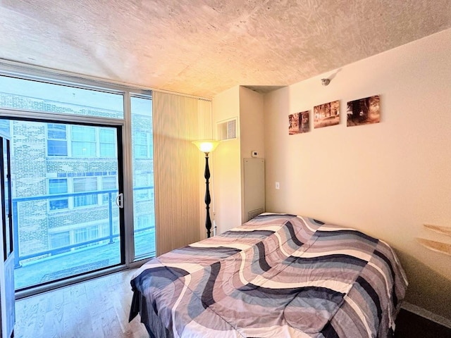 bedroom with access to exterior, expansive windows, a textured ceiling, and wood-type flooring